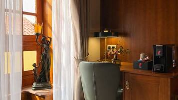 A room with a wooden desk, a chair, a statue, a lamp, and a coffee machine.