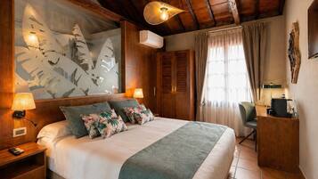 Un dormitorio con cama, mesitas de noche, escritorio, silla, ventana grande con cortinas y ventilador de techo.