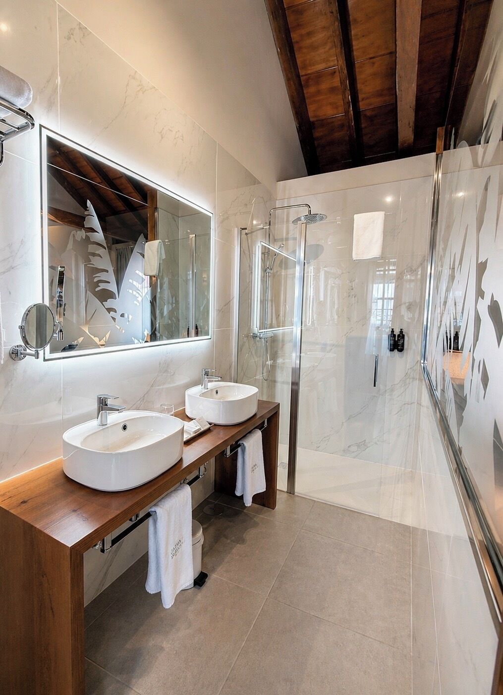 Ein modernes Badezimmer mit zwei Waschbecken, einer Duschkabine aus Glas und einem großen Spiegel.