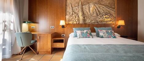 A hotel room with a bed, desk, chair, lamps, and a large wall painting.