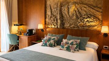 Habitación de hotel con una cama grande, dos mesitas de noche, un escritorio con silla, un mural grande en la pared y vistas al exterior.