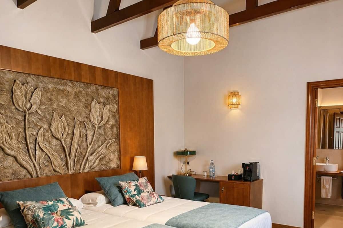 Un lit double avec une tête de lit, une table de chevet avec une lampe, un luminaire fixé au mur et un plafond en bois.