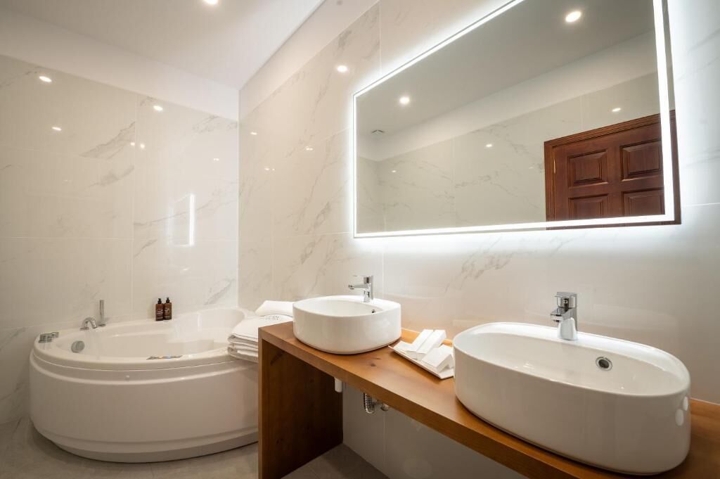 Een moderne badkamer met een ruime badkuip, twee wasbakken en een spiegel met ingebouwde verlichting.