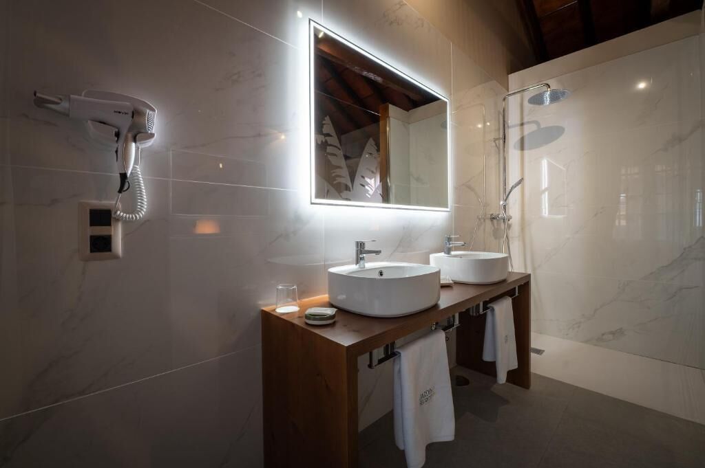 Ein modernes Badezimmer mit einem großen Spiegel, zwei Waschbecken, einem Fön und einer Dusche.