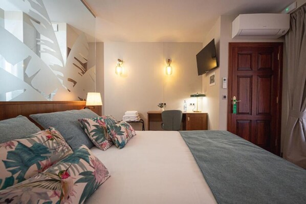 A hotel room with a bed, a desk, a chair, a TV, and an air conditioning unit. - Hotel Jardin Secreto (La Orotava)