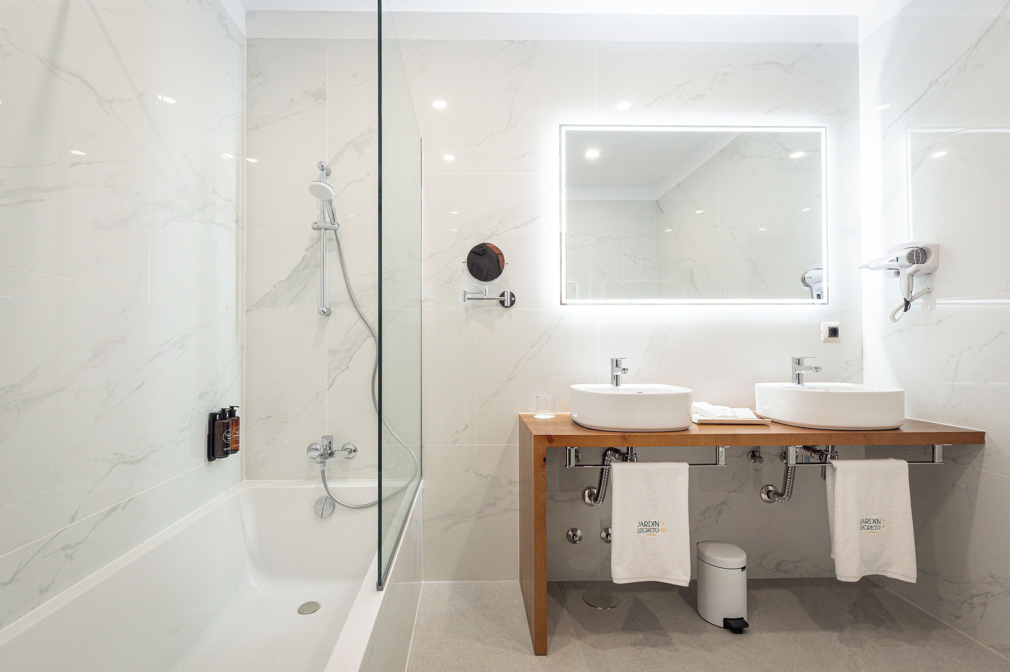 Un baño moderno con ducha de vidrio, dos lavamanos, un espejo y un perchero para toallas.
