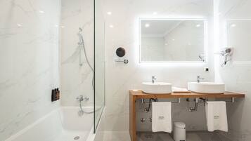Un baño moderno con ducha de vidrio, dos lavamanos, un espejo y un perchero para toallas.