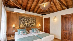 Ein Doppelzimmer mit zwei Betten, Holzbalkendecke, einem großen Blumenbild, Wandleuchten und einer Holztür.