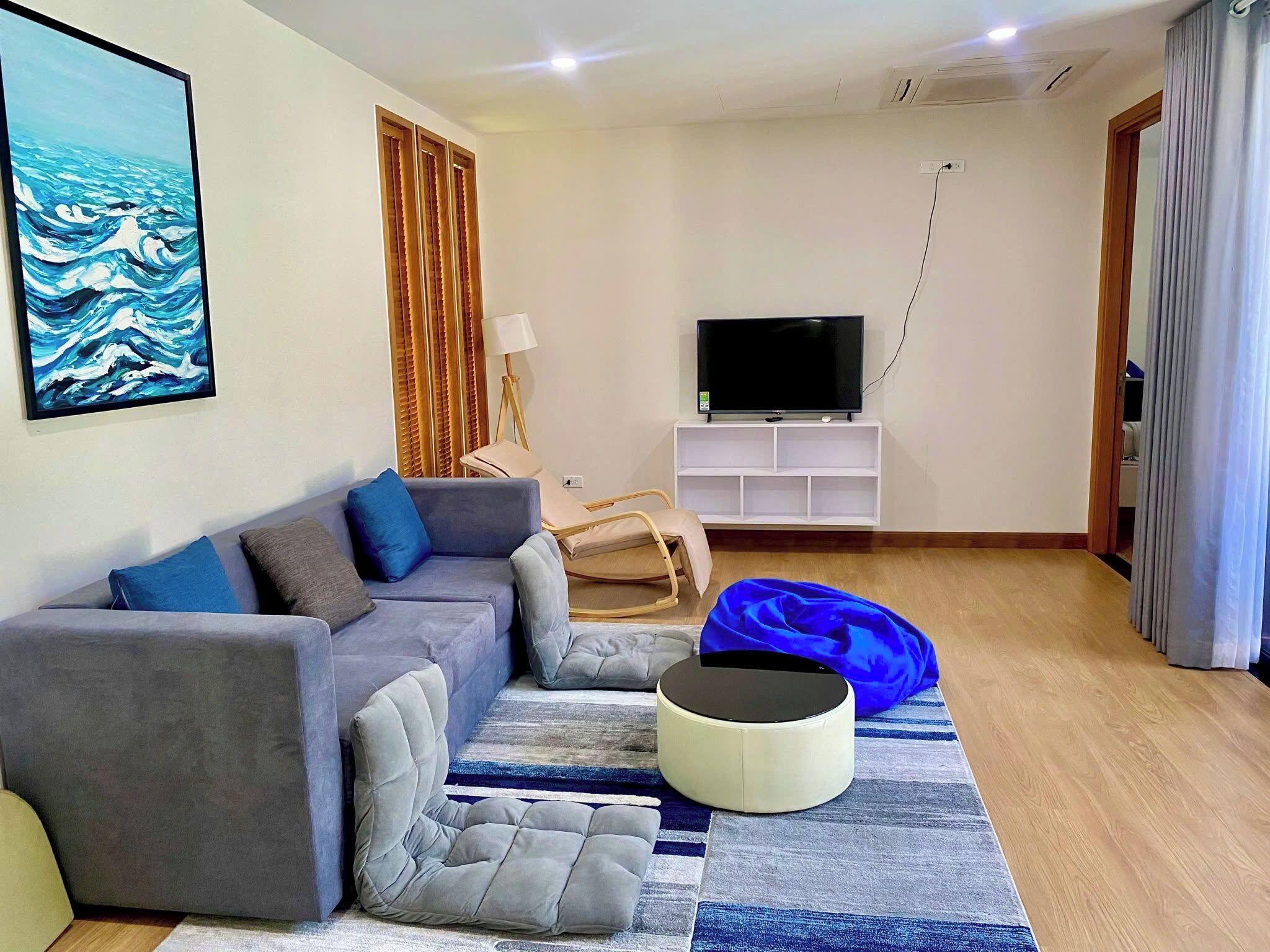 A living room with a sofa, a television on a stand, a lamp, and a blue bean bag.