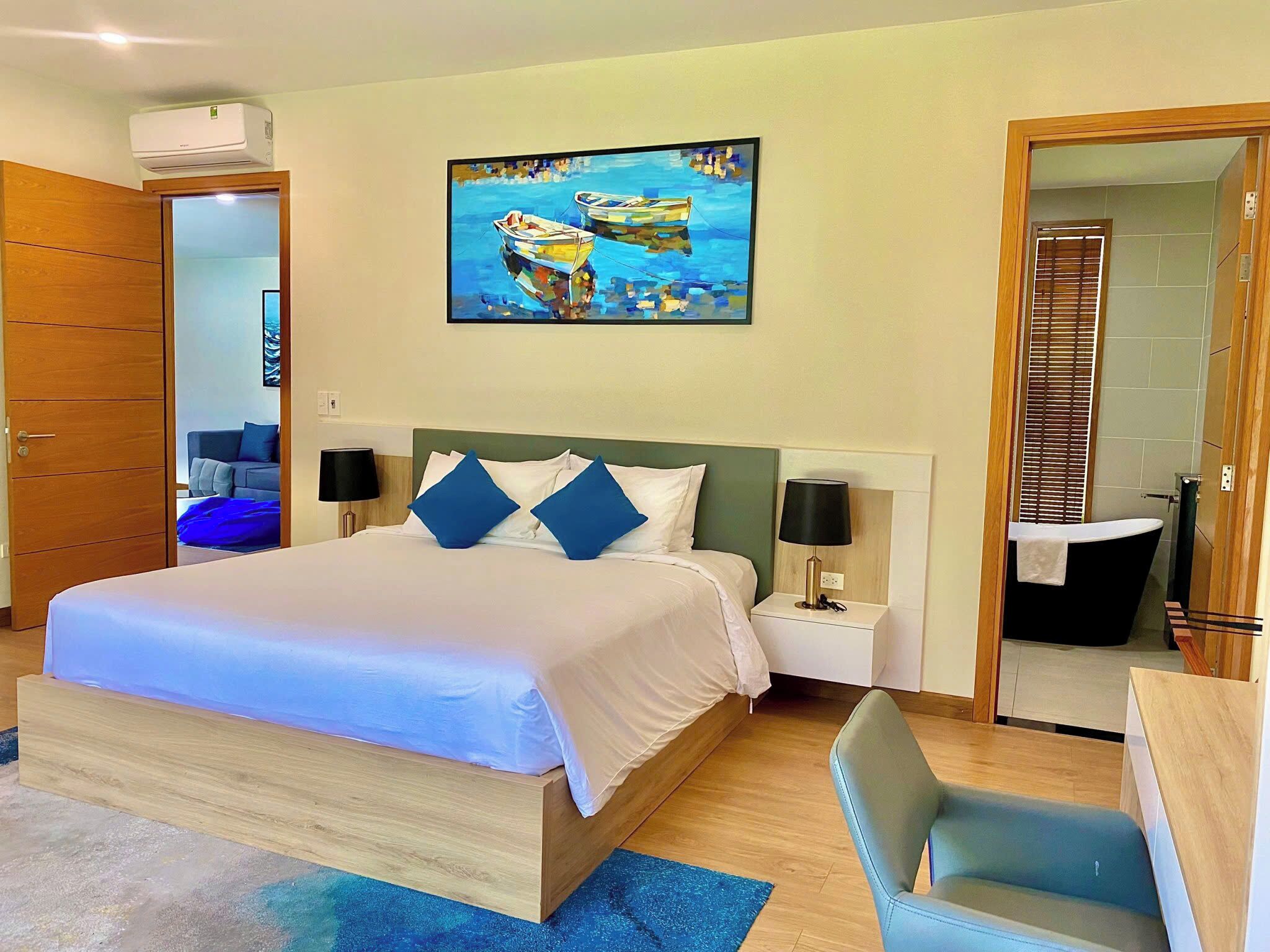 Une chambre d’hôtel avec un grand lit, deux tables de chevet, un tableau, une salle de bain avec baignoire et une armoire en bois.