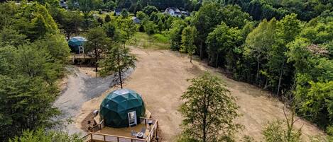 A large dome-shaped tent with a deck and seating area, surrounded by dense forest and a mountain in the background.