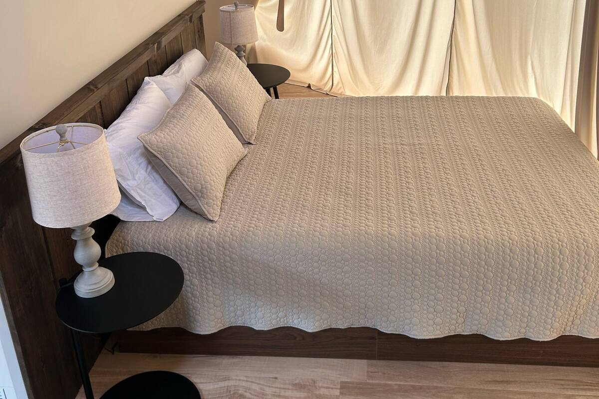 A bed with a textured blanket, a bedside lamp, and a small round table.