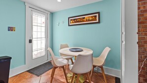Un coin repas avec une table ronde et quatre chaises, un tableau encadré au mur et une porte avec une fenêtre.