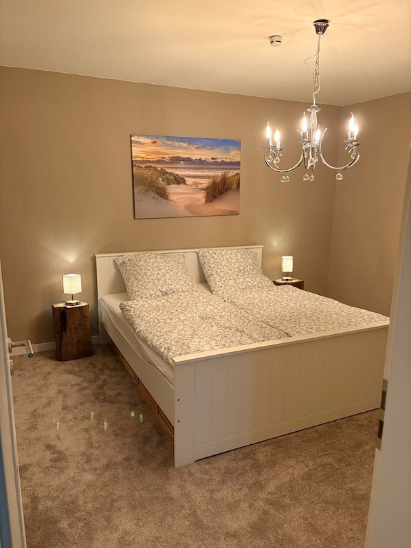 Une chambre à coucher comprenant un lit, une table de chevet, une lampe, un lustre et un tableau accroché au mur.