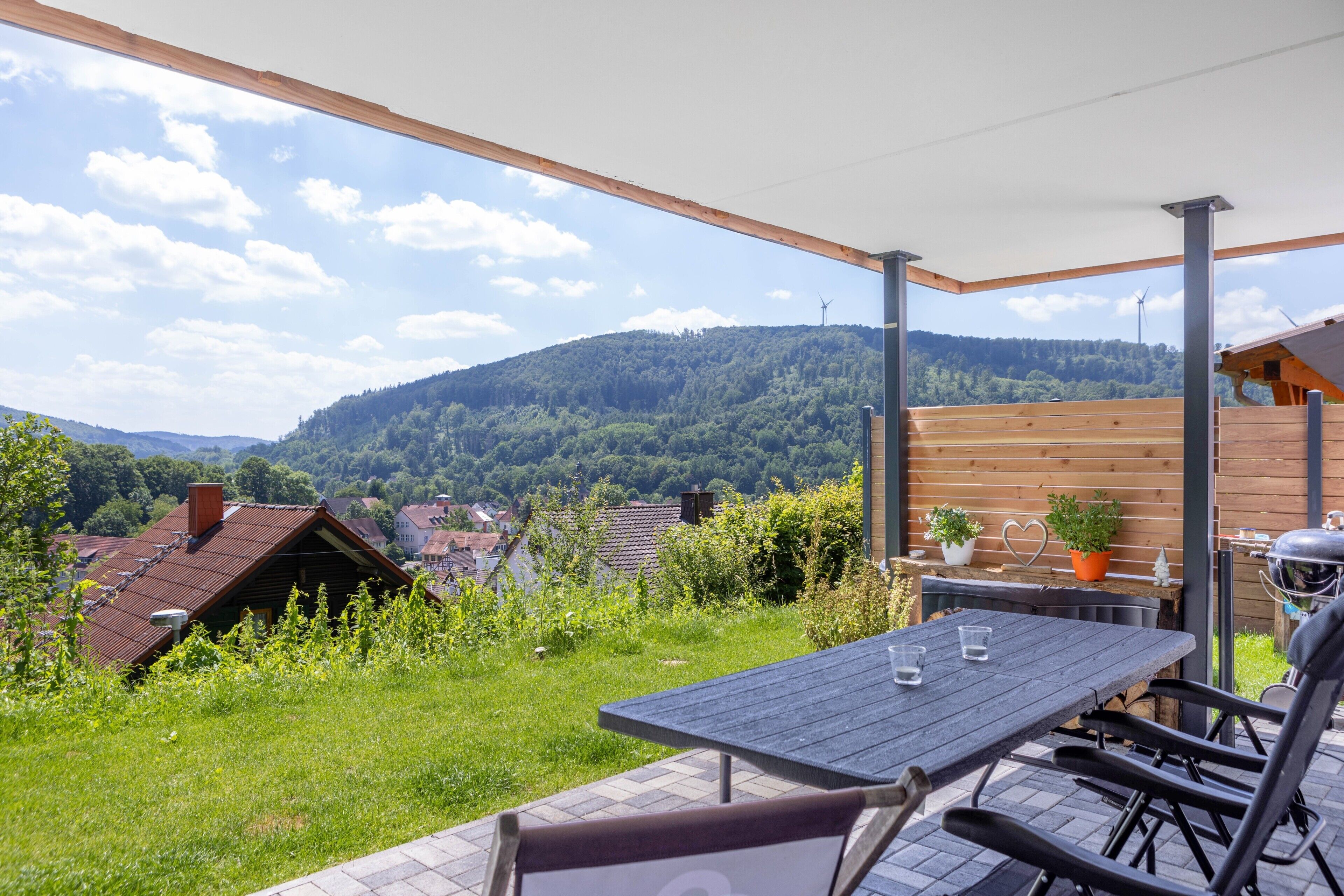 A patio with a table and chairs, a grill, and a view of a village and hills.