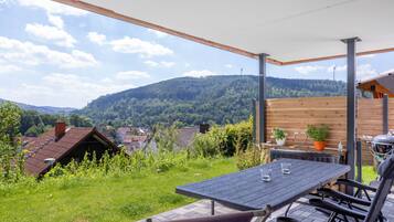A patio with a table and chairs, a grill, and a view of a village and hills.