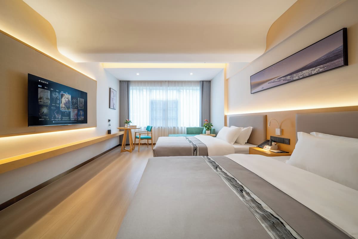 A hotel room with a TV, two beds, a desk, and a window with curtains.