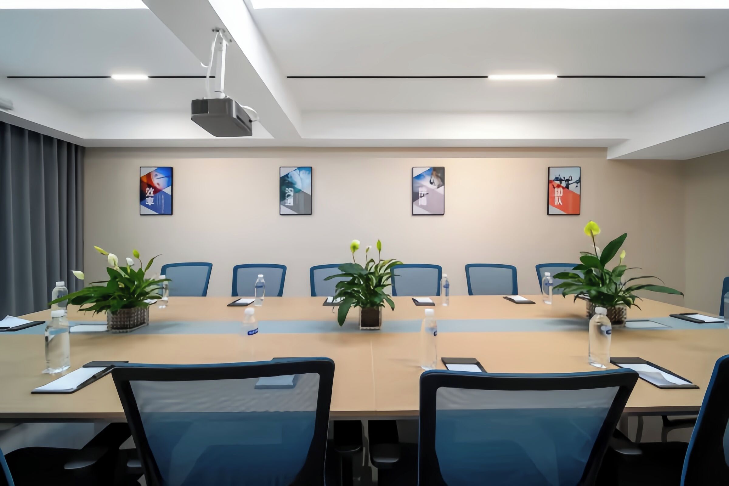 A conference room with a long table, chairs, potted plants, water bottles, and framed pictures on the wall.