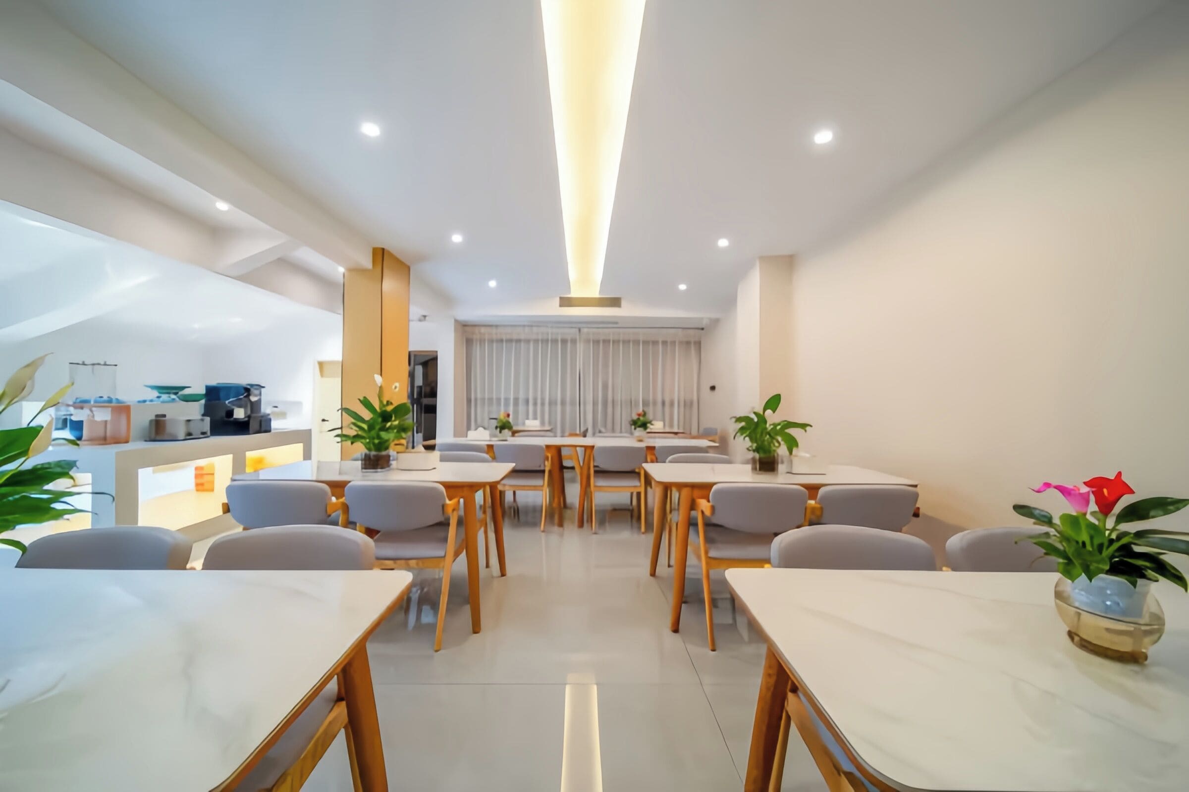 Een moderne hotel eetruimte met marmeren tafels, grijze stoelen en potplanten.