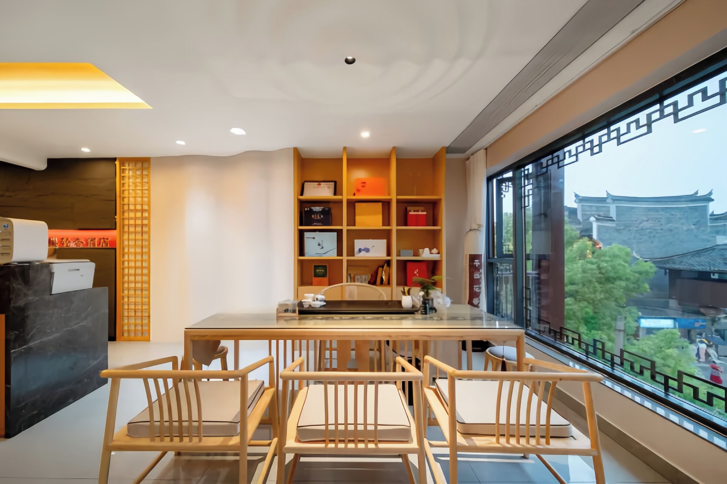 A modern interior with a dining area, wooden chairs, a glass table, and a view of traditional architecture.