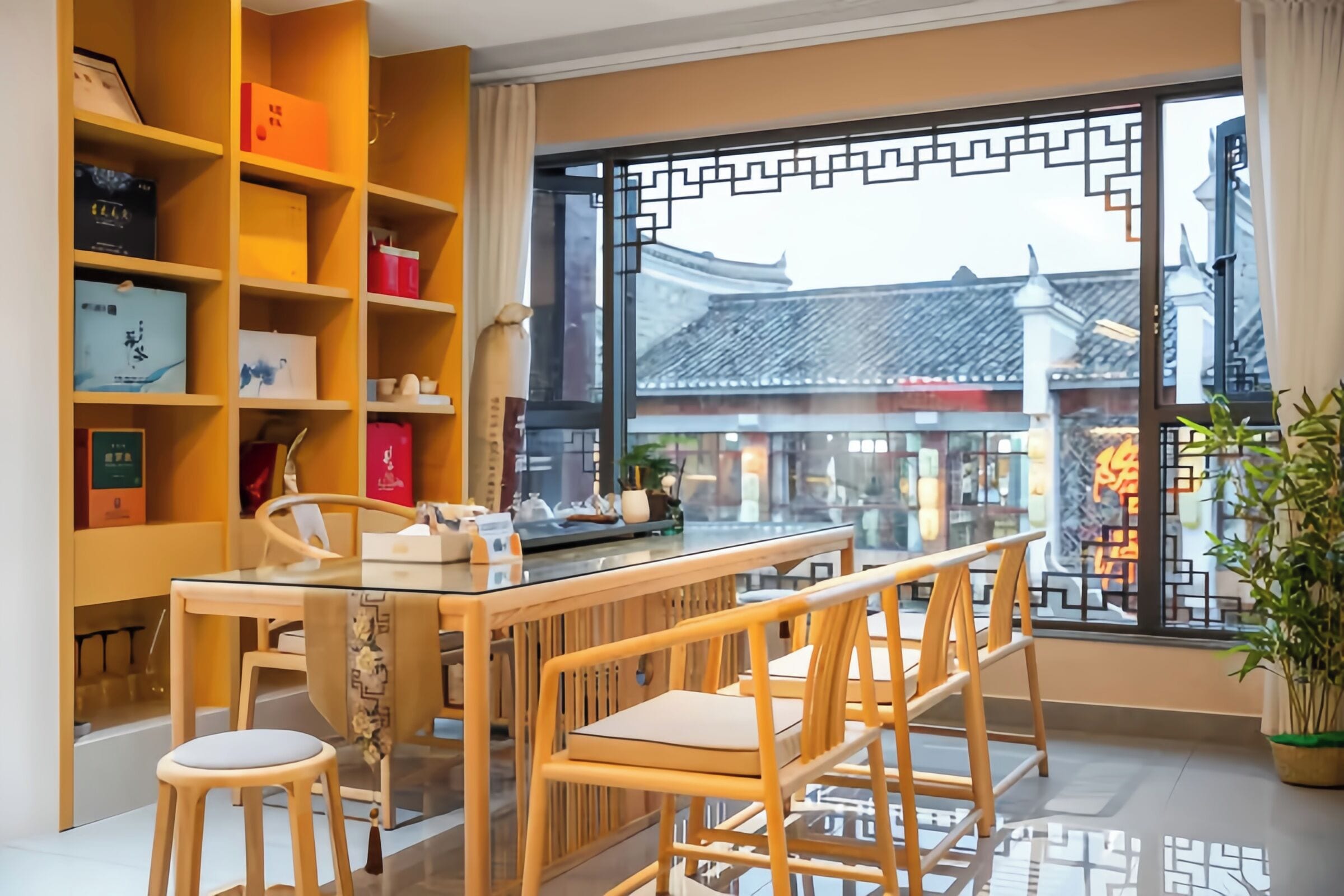 A dining area with a glass table, wooden chairs, and a view of traditional architecture through a window with a decorative screen.