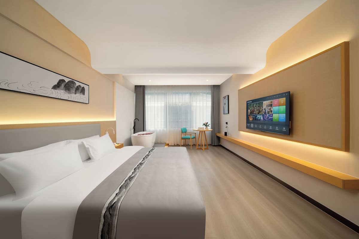 A modern hotel room with a large bed, a desk, a TV, and a painting on the wall.