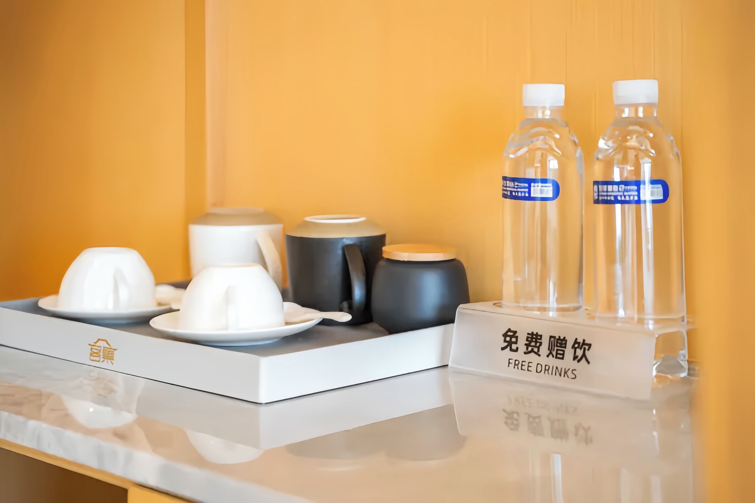 A hotel room's breakfast setup with a coffee maker, tea set, and two water bottles labeled 'FREE DRINKS'.