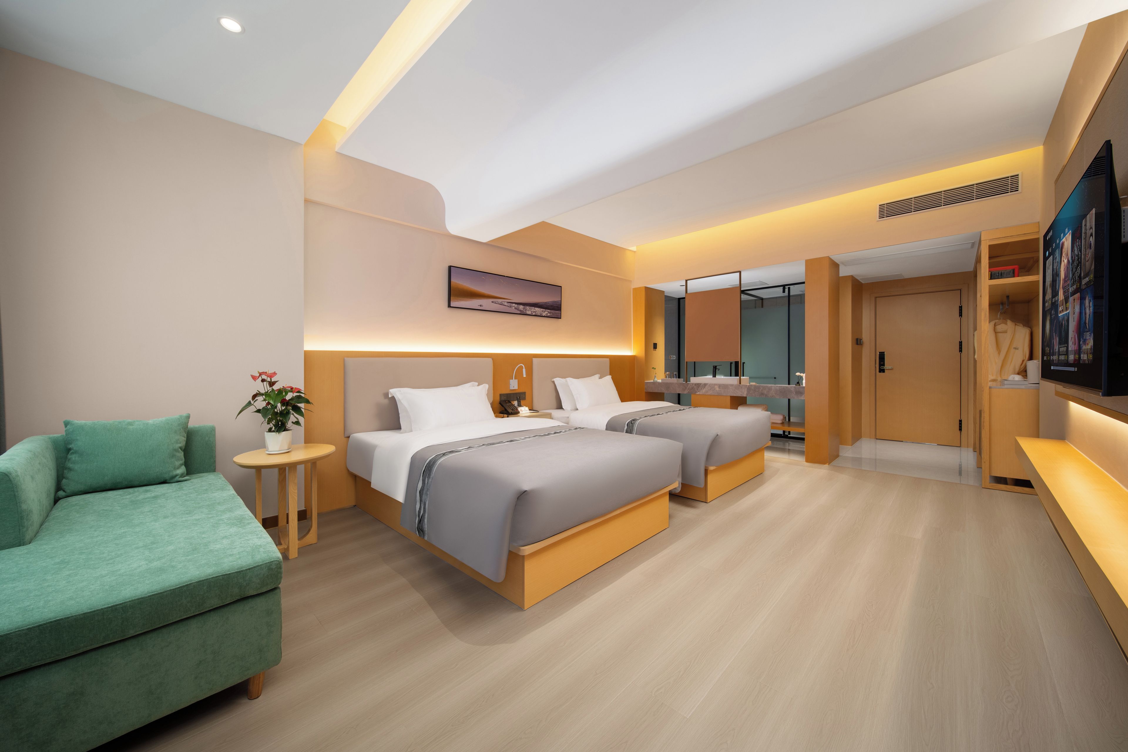 A modern hotel room with a sofa, two beds, a TV, and a small table with a plant.