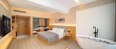 Una habitación de hotel moderna con una cama grande, zona de estar, baño con bañera y televisión.