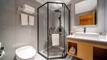 Un baño moderno con ducha acristalada, lavamanos blanco y espejo sobre él.