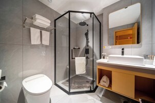 Un baño moderno con ducha acristalada, lavamanos blanco y espejo sobre él.