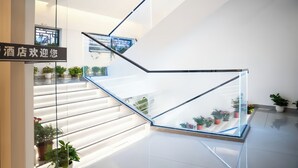 Een modern hotelinterieur met een glazen balustrade, plantenpotten en een bord dat gasten verwelkomt.