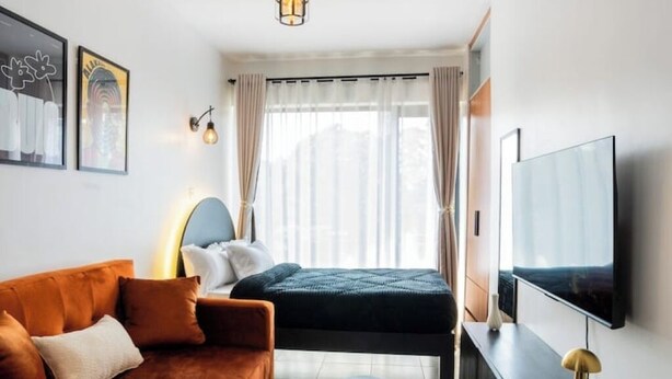 Moderni hotellihuone, jossa on sohva, sänky, televisio ja ikkuna, jossa on verhot.