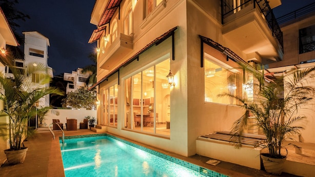 A swimming pool with tiled edges, adjacent to a building with large windows and a balcony. - Staymaster White Castle-4BHK (Vagator)