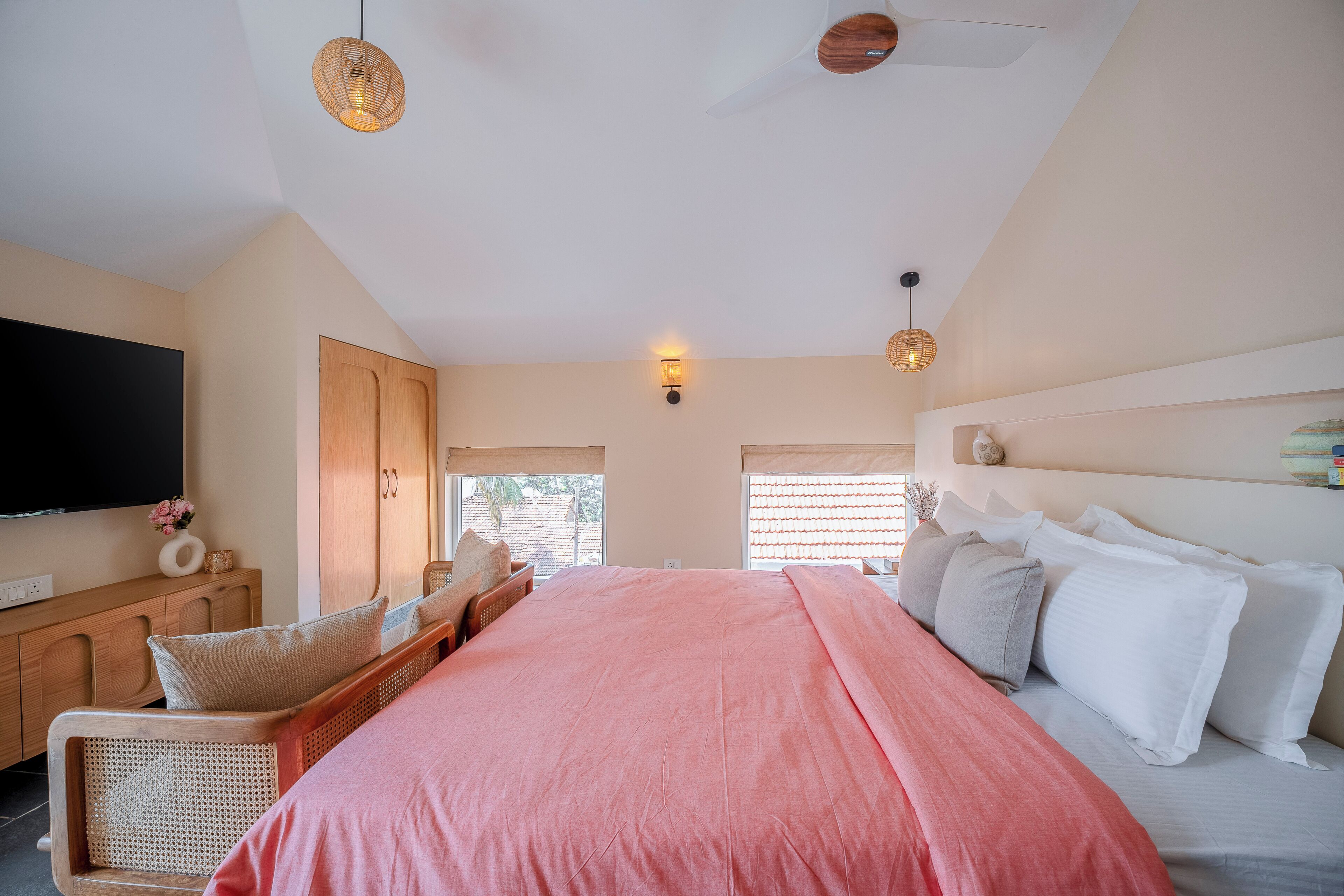 A bedroom with a bed, a TV, a wooden cabinet, and a wicker chair.