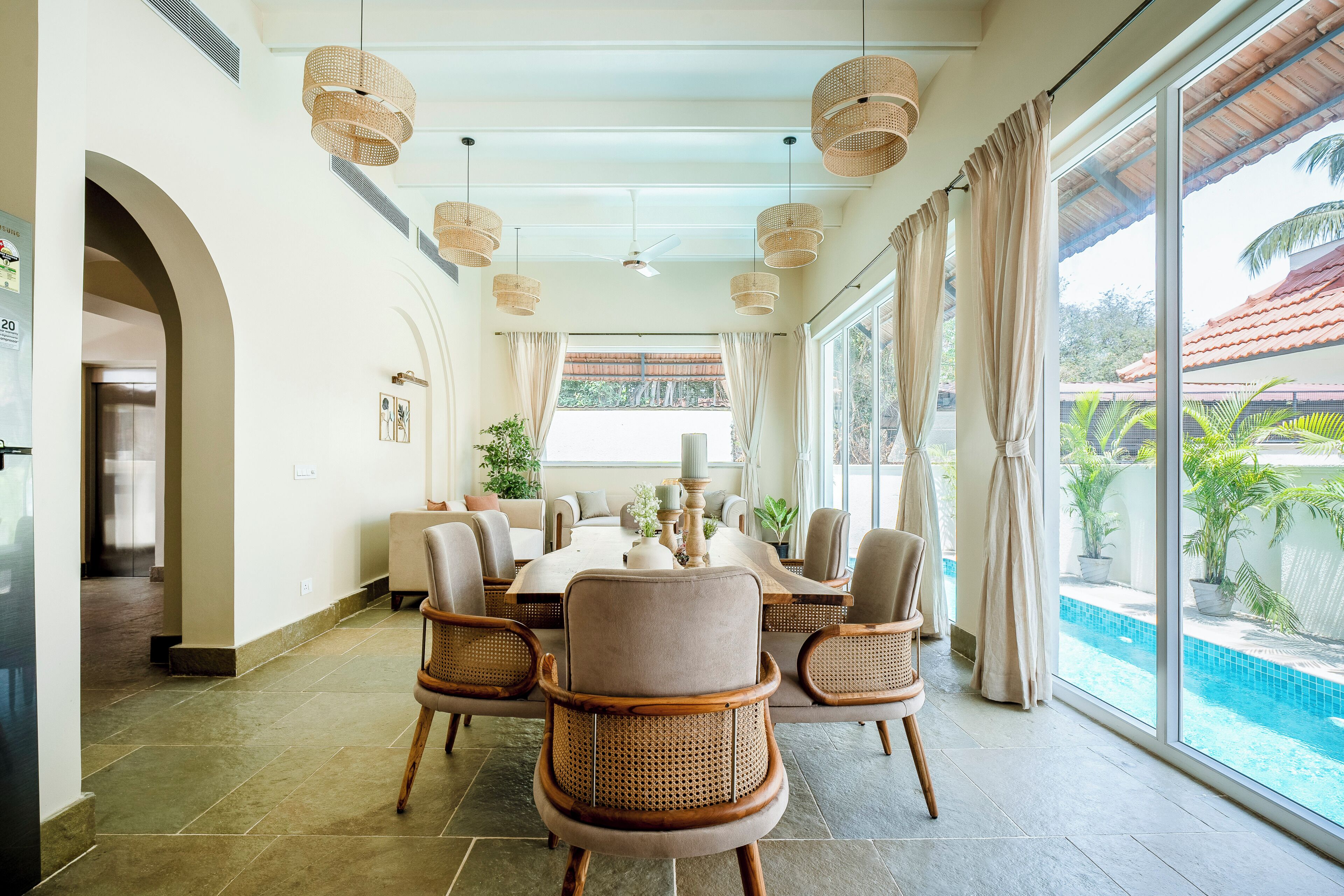 Un comedor con una mesa redonda, sillas de mimbre y vista a una piscina.