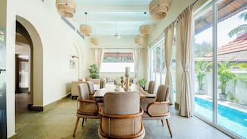 Un comedor con una mesa redonda, sillas de mimbre y vista a una piscina.