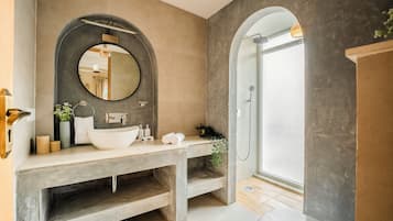 A modern bathroom with a large round mirror, a vessel sink, and a shower area.
