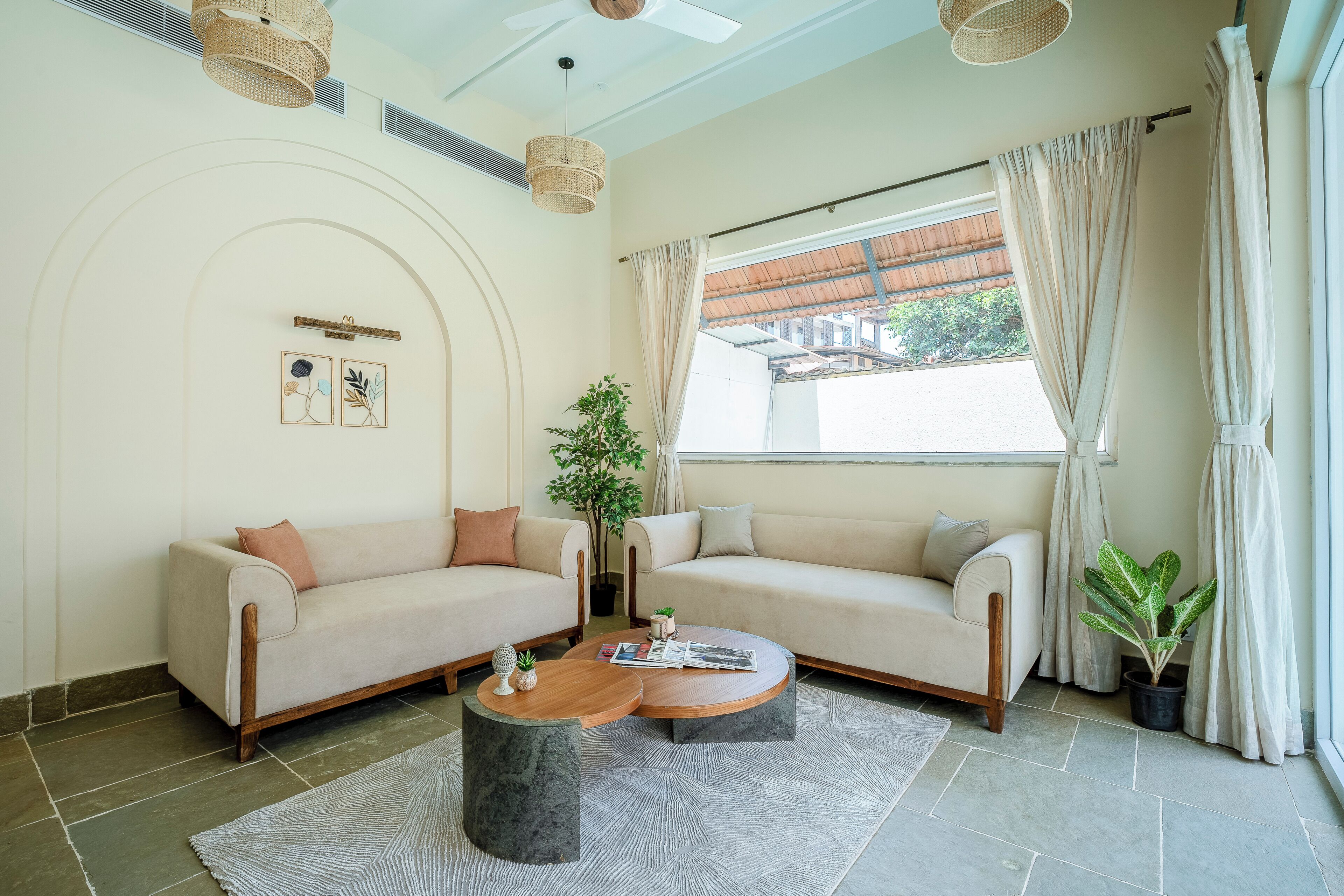 Ein Wohnzimmer mit zwei Sofas, einem Couchtisch, einer Topfpflanze und einem großen Fenster mit Vorhängen.