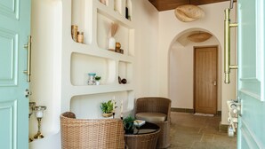 A hallway with wicker furniture, shelves with decorative items, and a wooden door. - Staymaster White Castle-4BHK (Vagator)