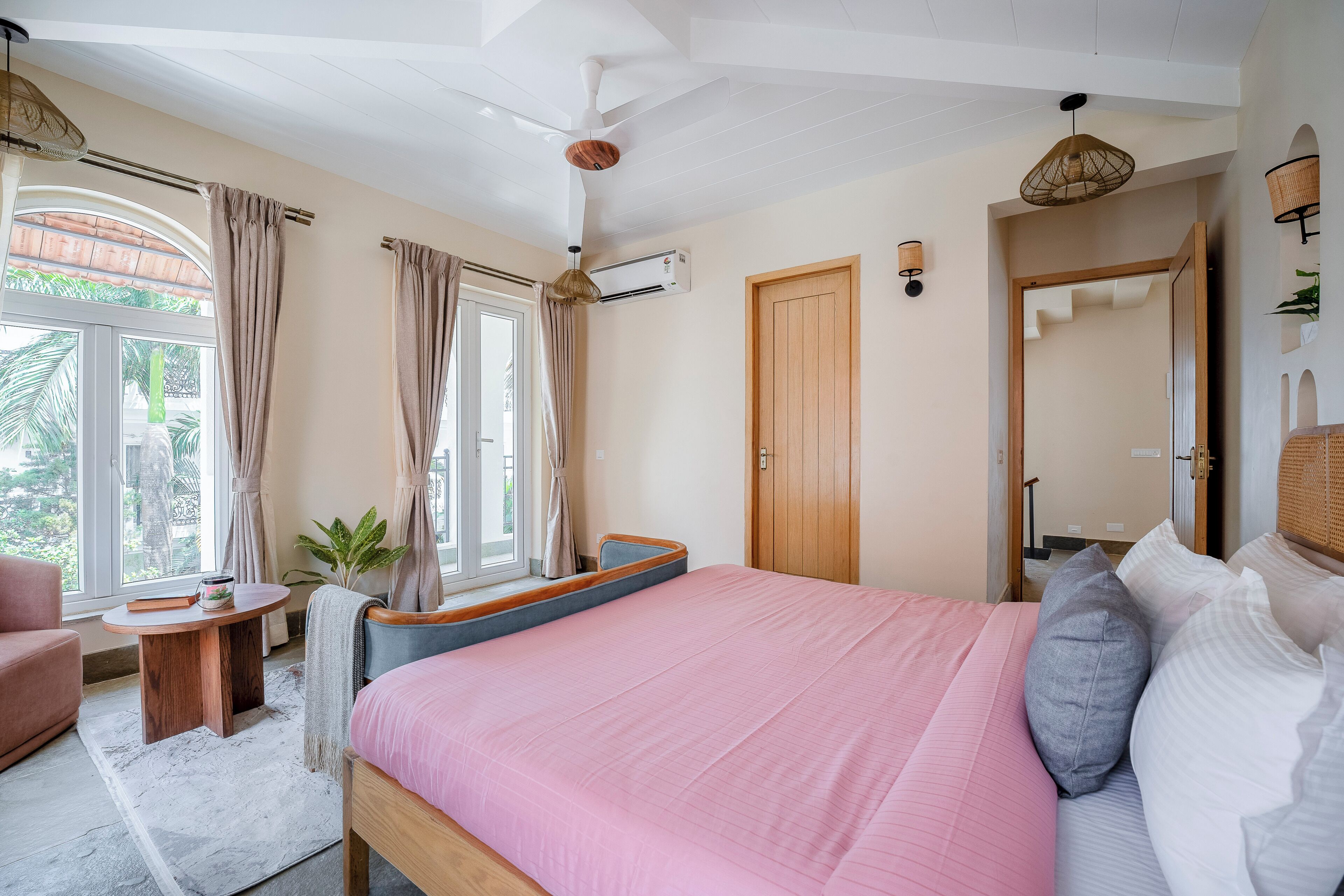A bedroom with a bed, a window with curtains, a ceiling fan, and a small table.