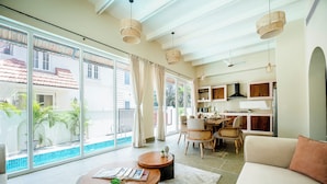 A spacious living area with a large window, a dining area, and a kitchen. - Staymaster White Castle-4BHK (Vagator)
