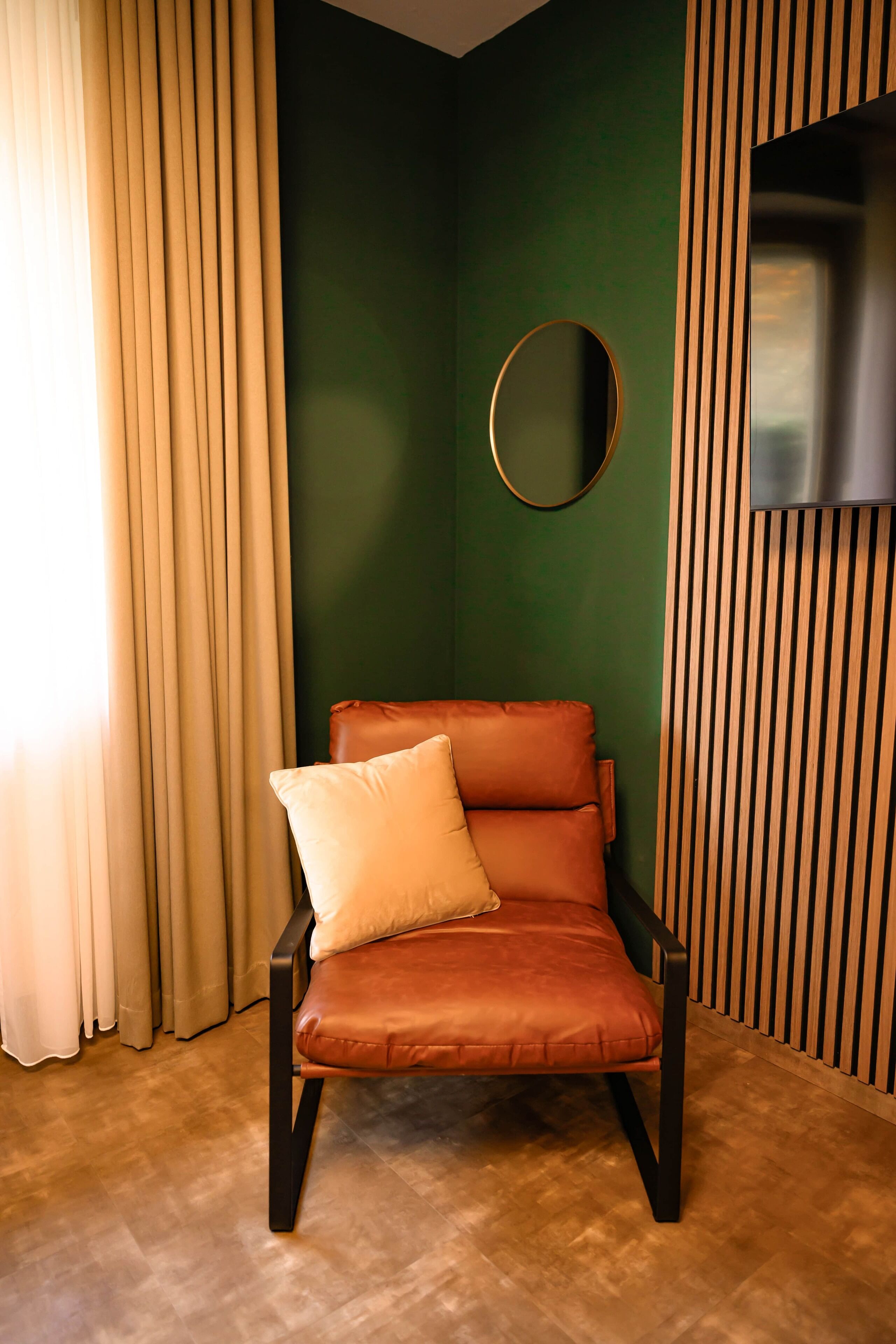 A room with a brown leather chair, a round mirror, and a television on a wooden panel wall.