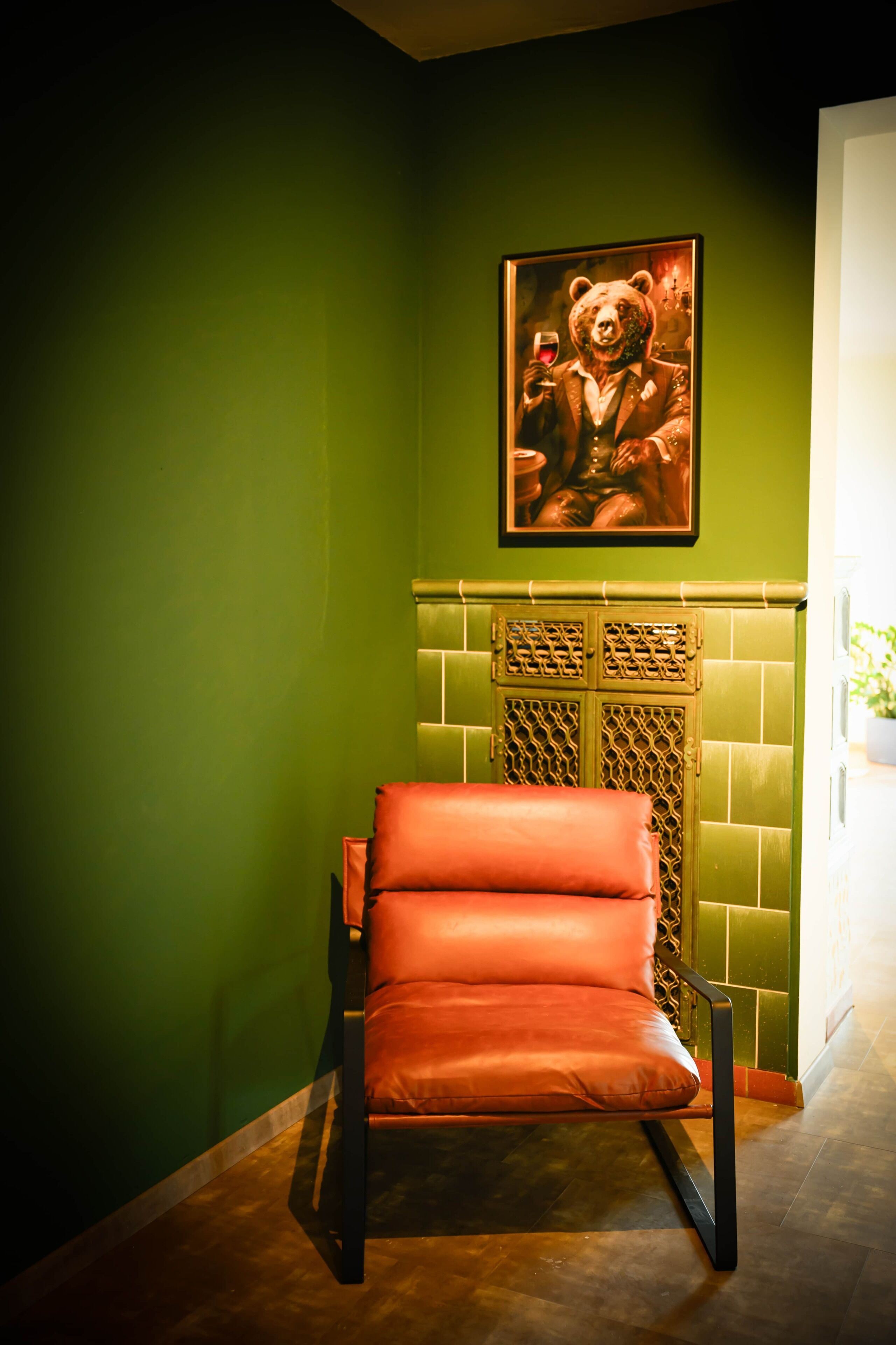 Una stanza con un muro verde, un quadro con un orso, una poltrona in pelle rossa e un camino decorato.