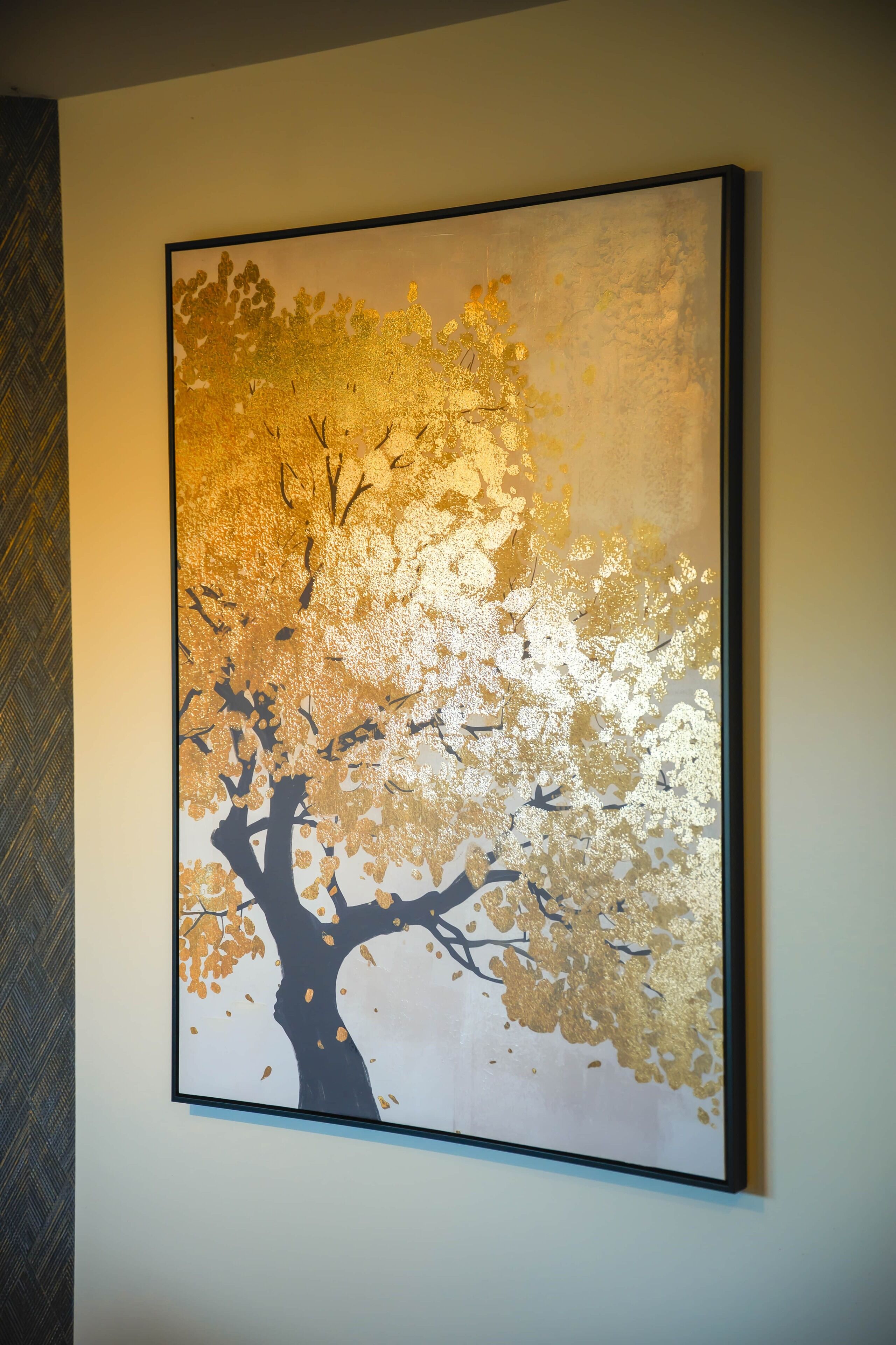 Une œuvre d’art encadrée représentant un arbre aux couleurs or et noir, accrochée à un mur.
