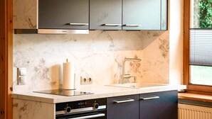 Une cuisine moderne avec des meubles de couleur sombre, un four encastré et une fenêtre équipée de stores.