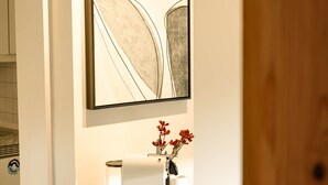 A modern kitchen with a white table, two chairs, a vase with red flowers, and a framed abstract painting on the wall. - SECHSER - Easy Apartment (Spalt)