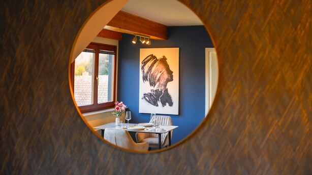 A dining area with a table set for two, a painting on the wall, and a window with a view of the outside. - VIERER - Cozy Apartment XL (Spalt)