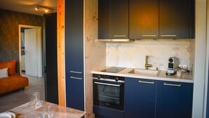 A modern kitchen with dark cabinetry, a built-in oven, and a countertop with a coffee machine. - VIERER - Cozy Apartment XL (Spalt)
