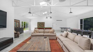 Ein großzügiges Wohnzimmer mit einer großen Couch, einem Couchtisch und einem Billardtisch. Ein Fernseher ist an der Wand montiert und über der Couch hängt ein Gemälde.